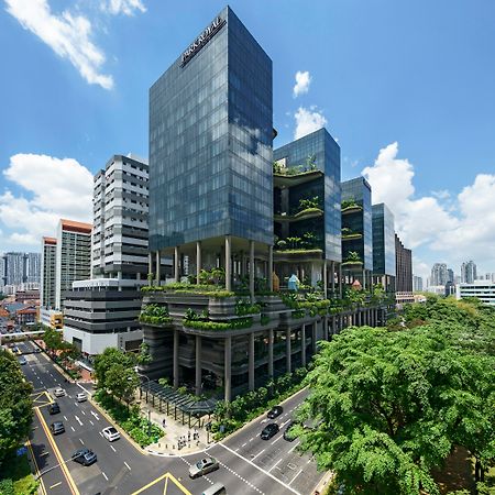 Parkroyal Collection Pickering, Singapura Luaran gambar The photo shows a modern urban architecture scene featuring several sleek glass buildings. These structures are complemented by greenery, with plants and trees integrated into their design, creating a lush environment. The scene includes a busy road 