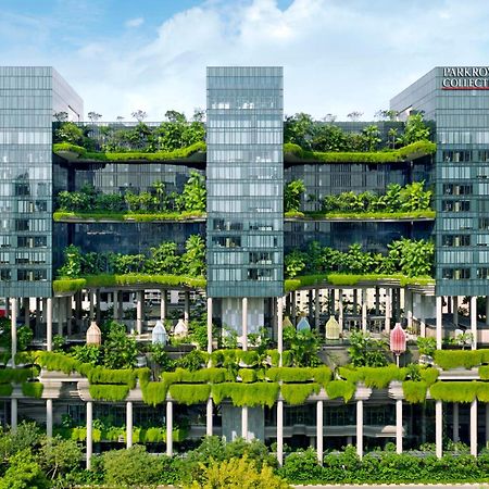 Parkroyal Collection Pickering, Singapura Luaran gambar The photo shows a modern multi-story building characterized by a sleek, glass facade. The structure features multiple floors with abundant greenery, including vertical gardens and terraces filled with plants, creating a striking contrast between the 