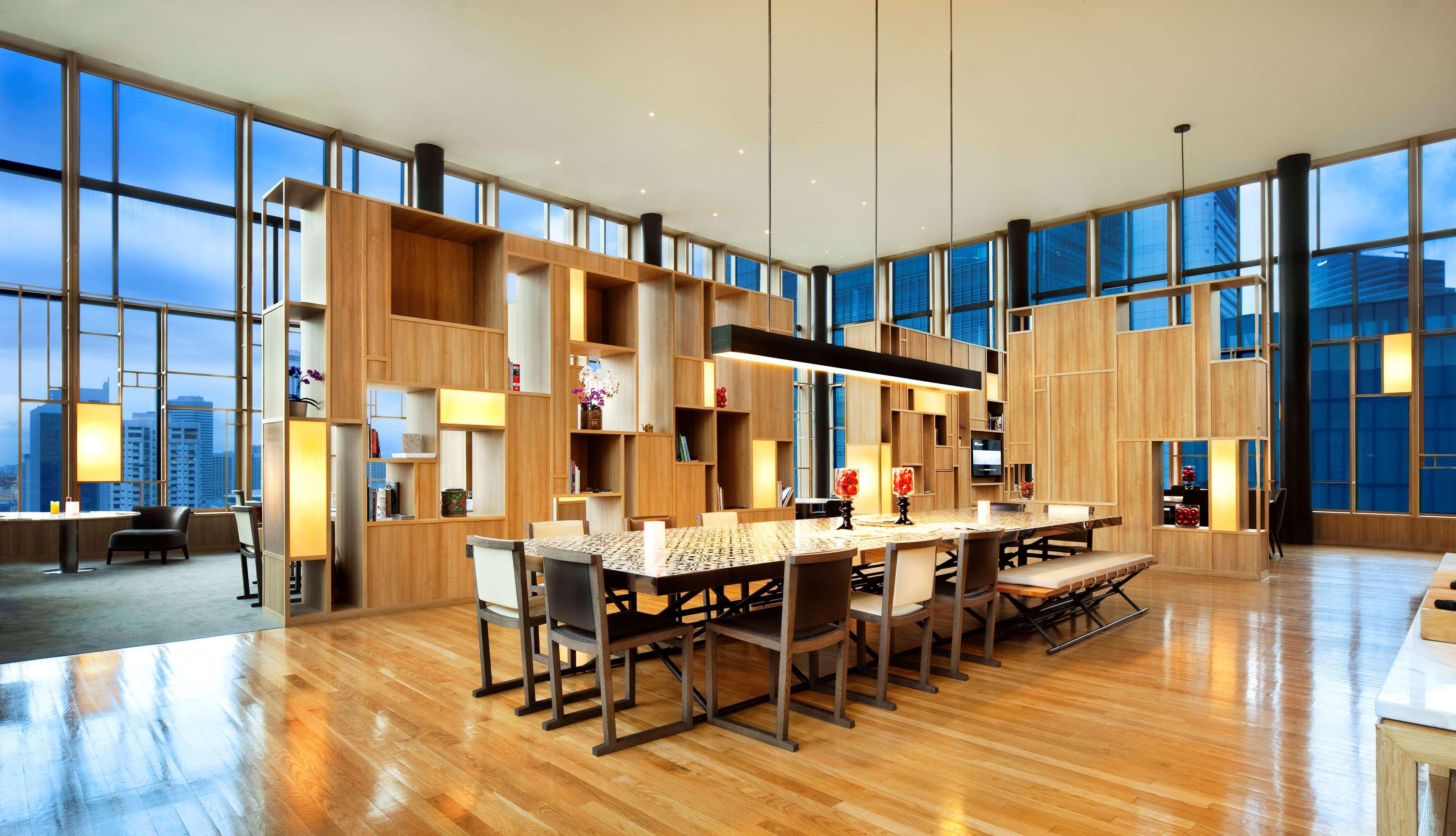 Parkroyal Collection Pickering, Singapura Luaran gambar The image shows a modern dining area or common space with an open layout. The room features large windows that allow natural light to flood in, enhancing the warm wooden tones of the décor. 

In the center, there is a long rectangular dining table su