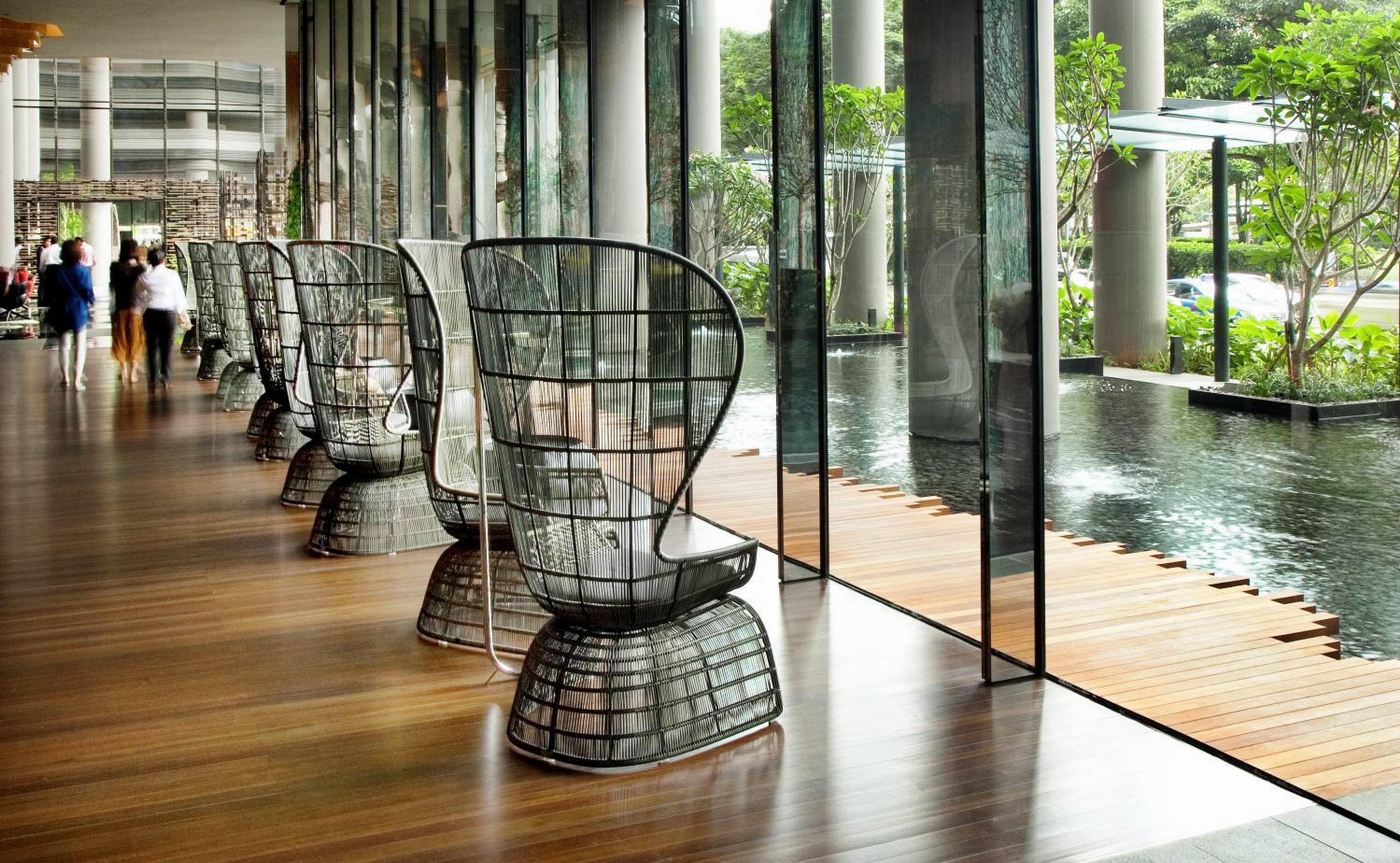 Parkroyal Collection Pickering, Singapura Luaran gambar The photo features a modern interior space with large glass windows that allow natural light to flood in. Along one side of the room, there are several distinctive black chairs with an open, lattice-like design. The flooring is made of polished wood,