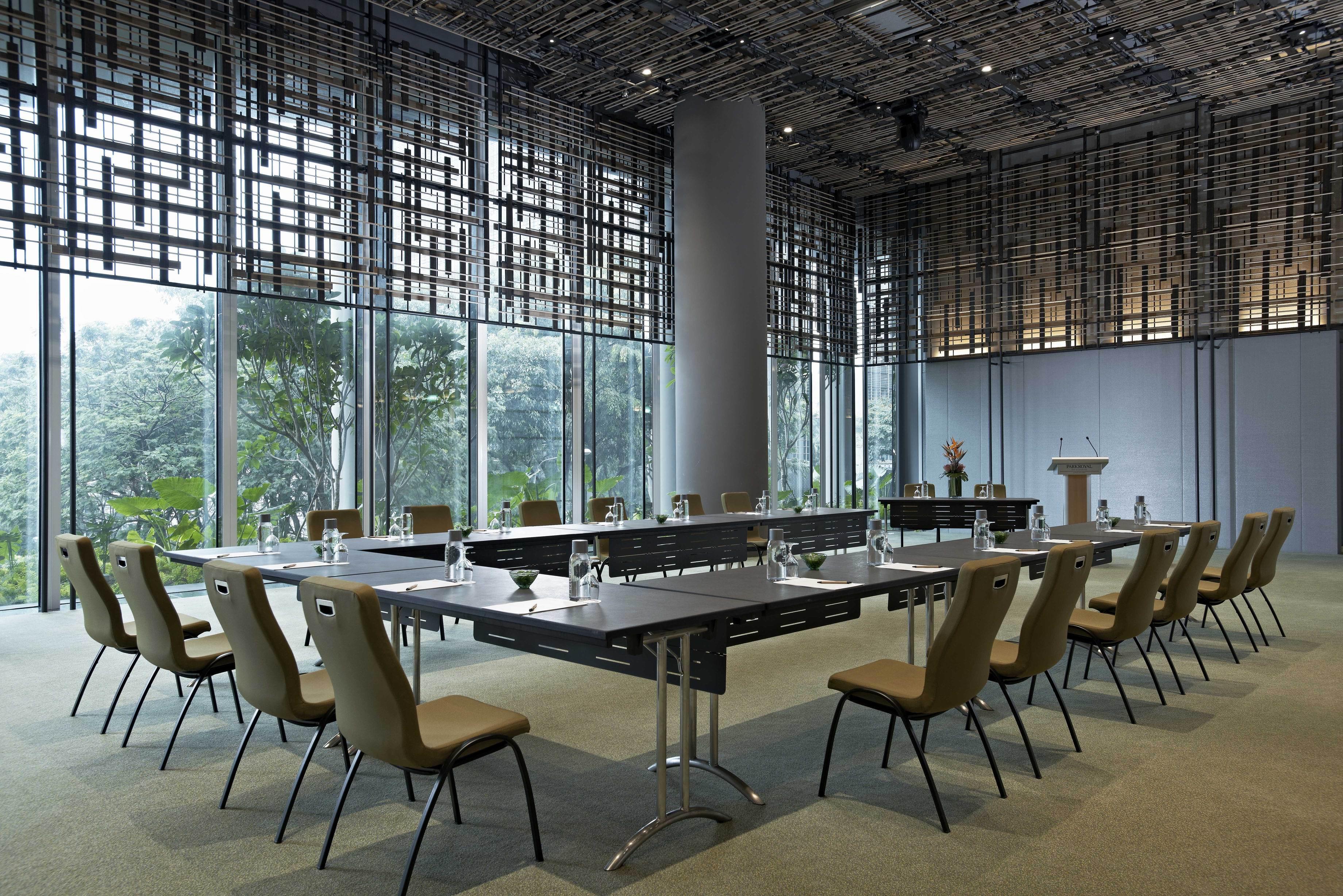 Parkroyal Collection Pickering, Singapura Luaran gambar The image shows a modern conference room. It features a long, rectangular table surrounded by several chairs. The table is equipped with glass water bottles and glasses. Large windows provide natural light and offer a view of greenery outside. The ro