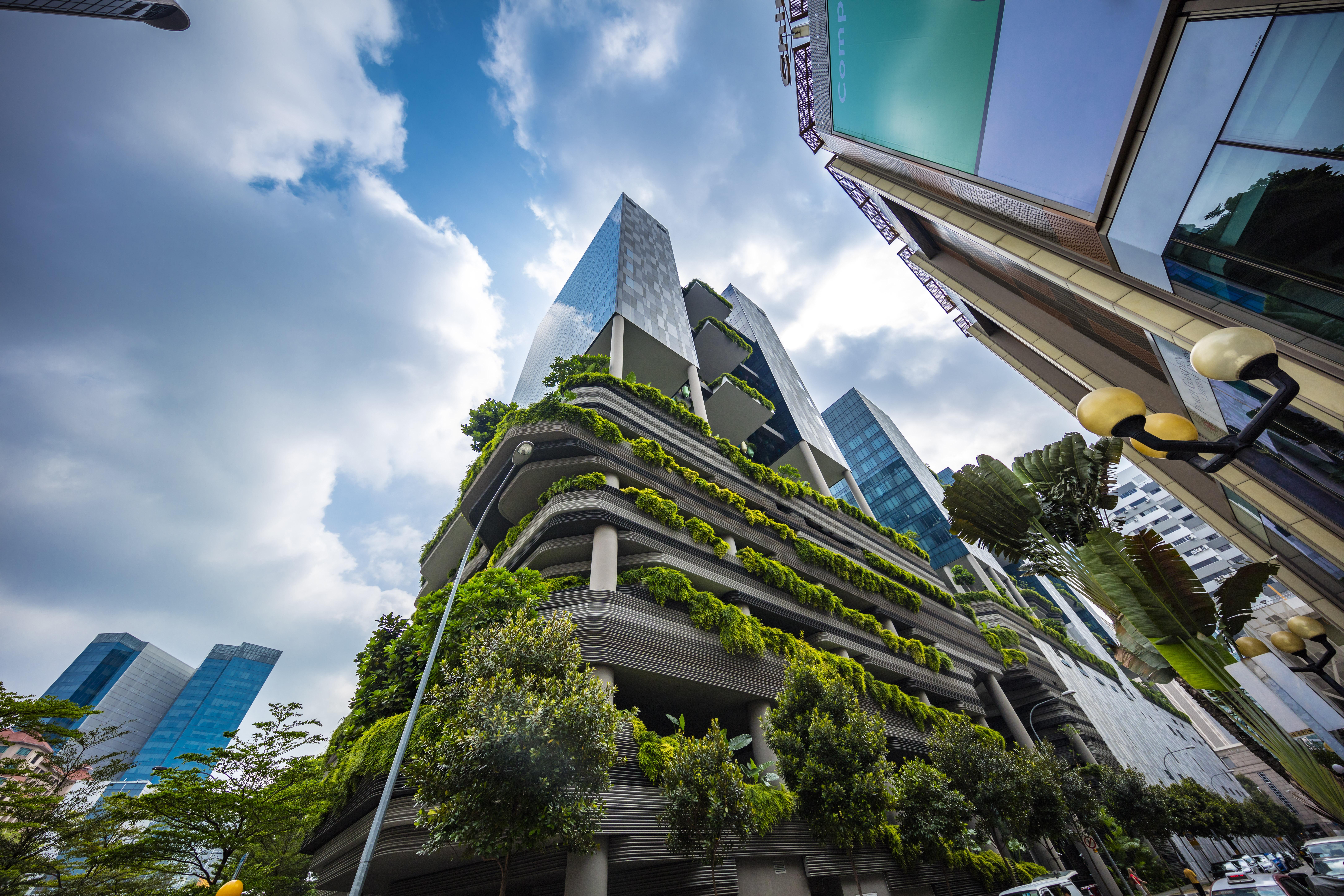 Parkroyal Collection Pickering, Singapura Luaran gambar The photo shows a modern urban setting featuring contemporary buildings. In the foreground, there is a distinctive structure with a green façade, showcasing various plants and greenery integrated into the architecture. The design appears to emphasize