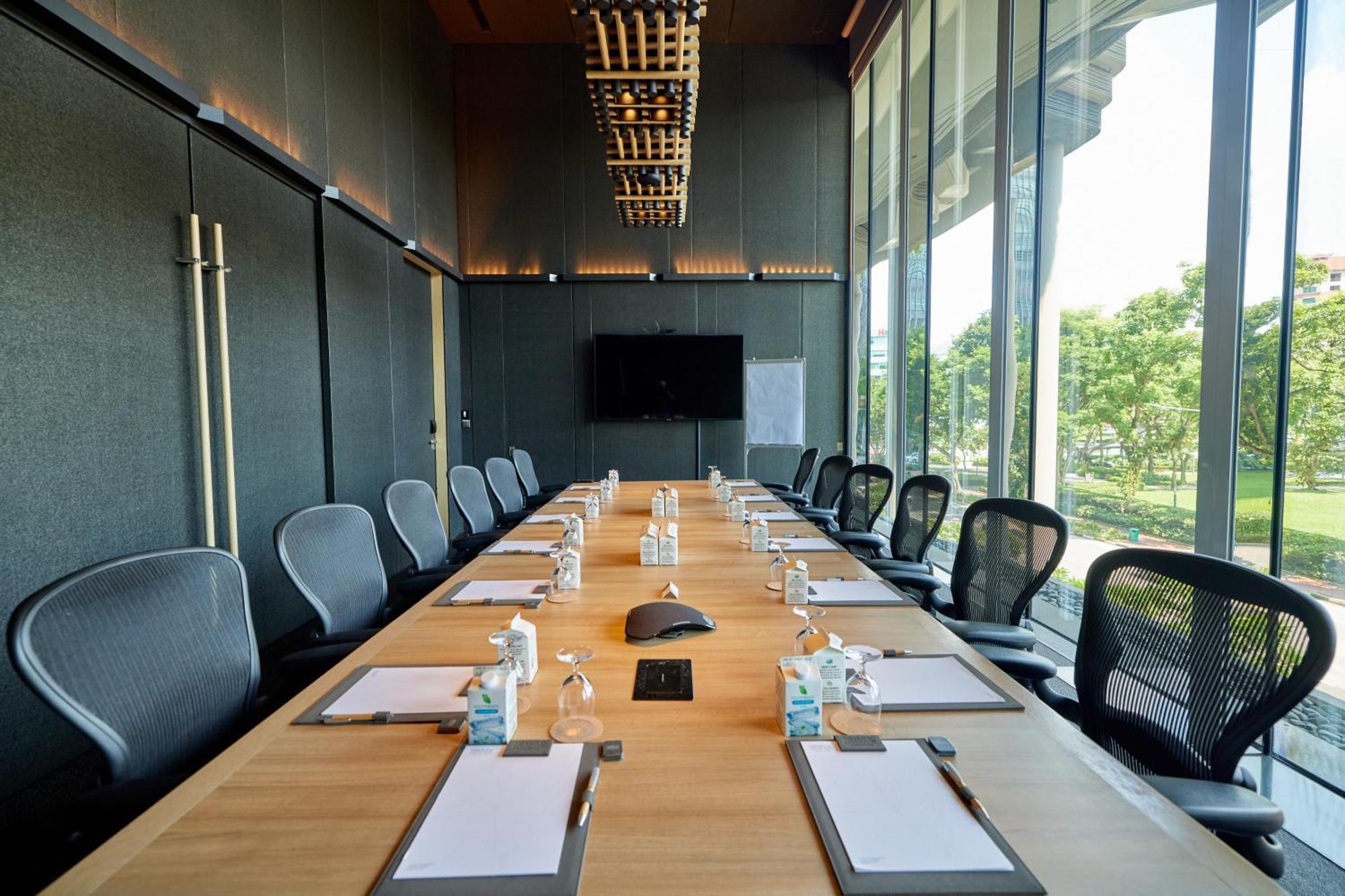 Parkroyal Collection Pickering, Singapura Luaran gambar The photo shows a modern conference room designed for meetings. It features a long wooden table surrounded by ergonomic chairs. On the table, there are several pieces of stationery, including notepads and pens, as well as small water bottles. A centr