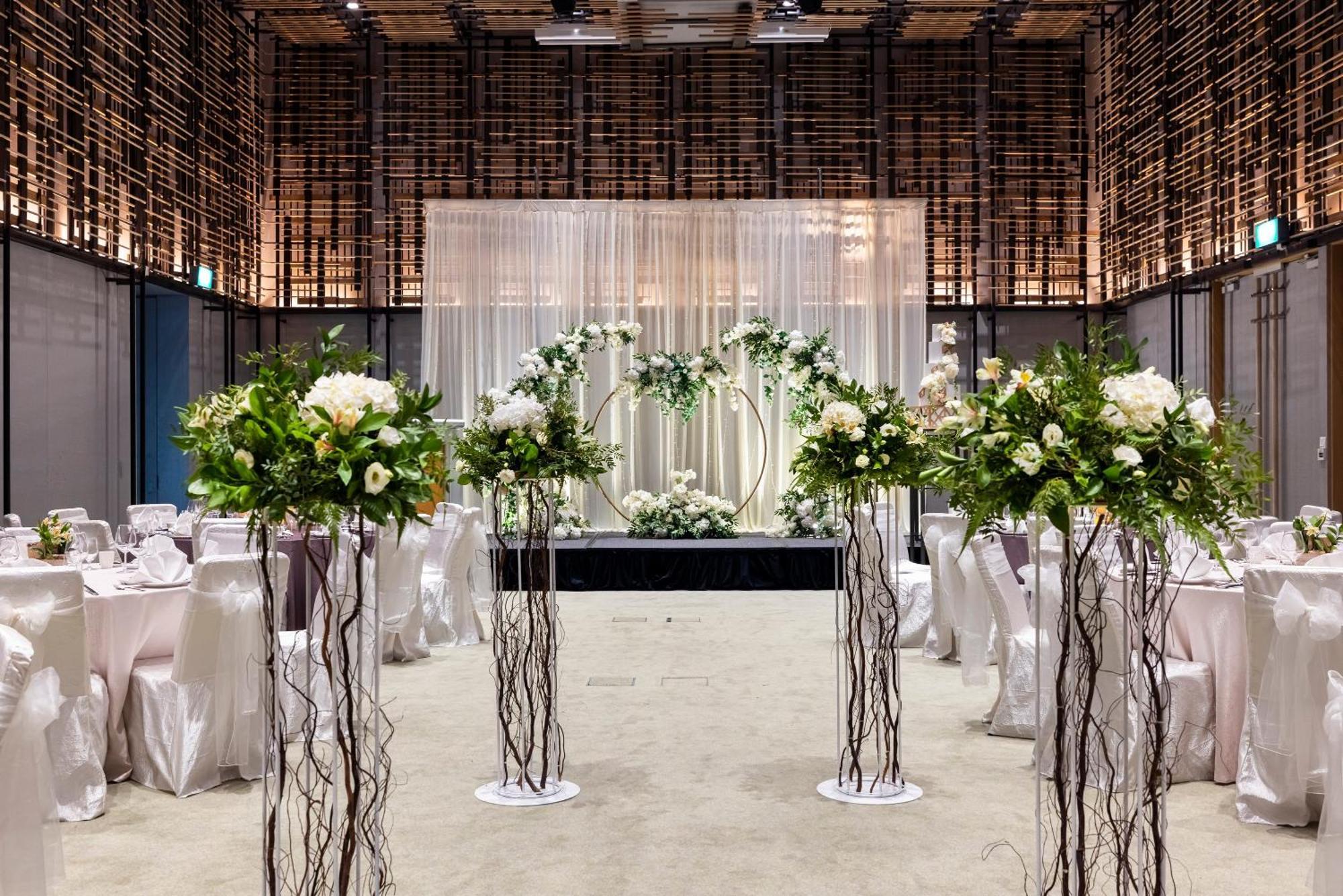 Parkroyal Collection Pickering, Singapura Luaran gambar The photo shows a beautifully decorated event space, likely set up for a wedding. In the center, there is an elegant backdrop made of draped fabric, creating a soft and romantic atmosphere. Flanking the backdrop are floral arrangements positioned on 