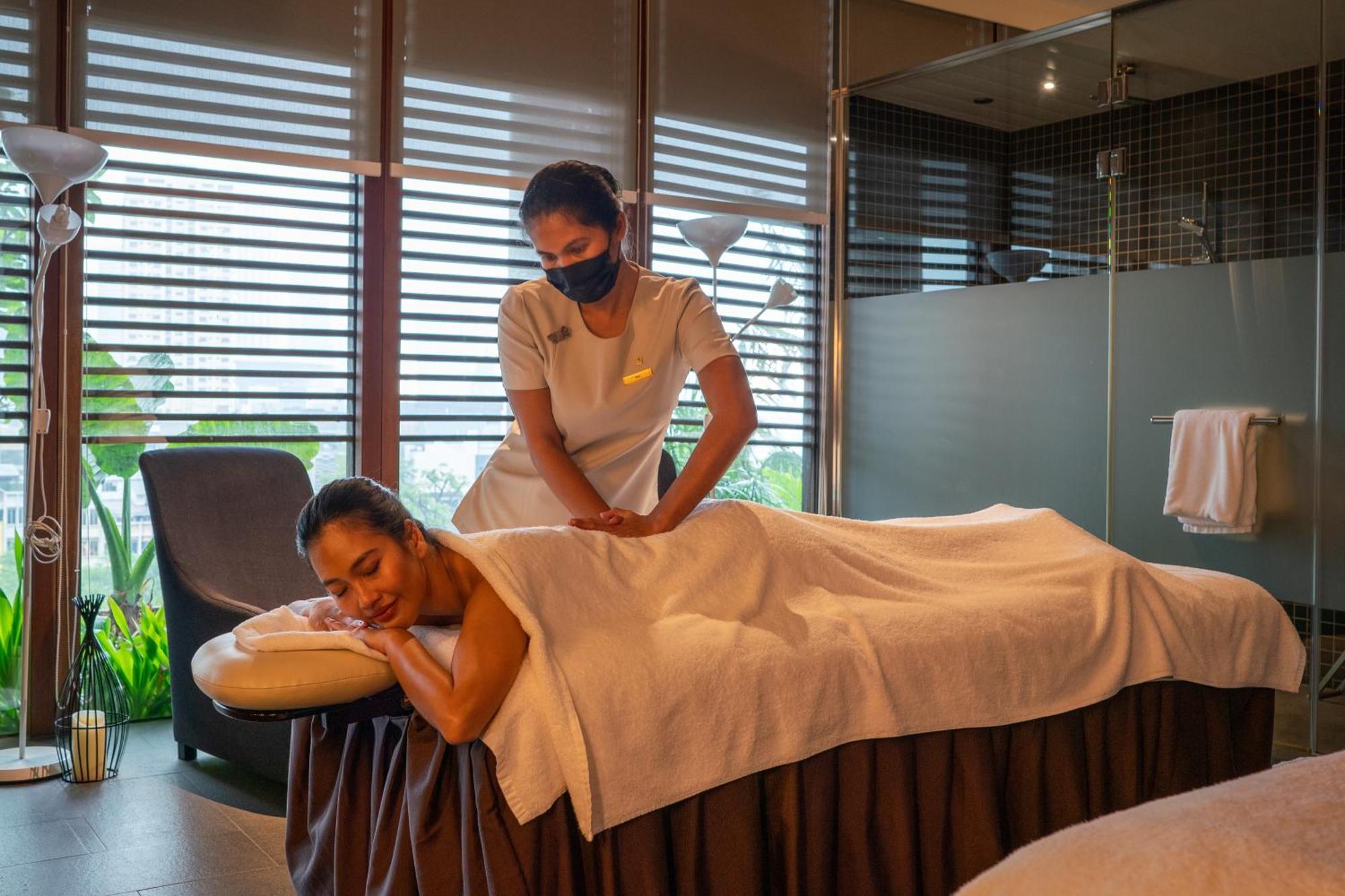 Parkroyal Collection Pickering, Singapura Luaran gambar The photo shows a serene spa setting where a therapist is giving a massage to a client. The client is lying face down on a massage table, covered with a towel, and appears to be relaxed. The therapist is positioned at the client's back, providing the