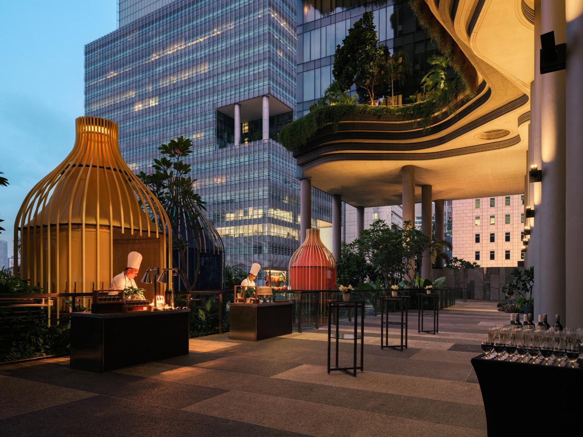 Parkroyal Collection Pickering, Singapura Luaran gambar The photo depicts an outdoor dining area that features modern architectural elements. Prominently visible are unique structures resembling large decorative enclosures in the shape of birdcages. Chefs can be seen working in these areas, presumably pre