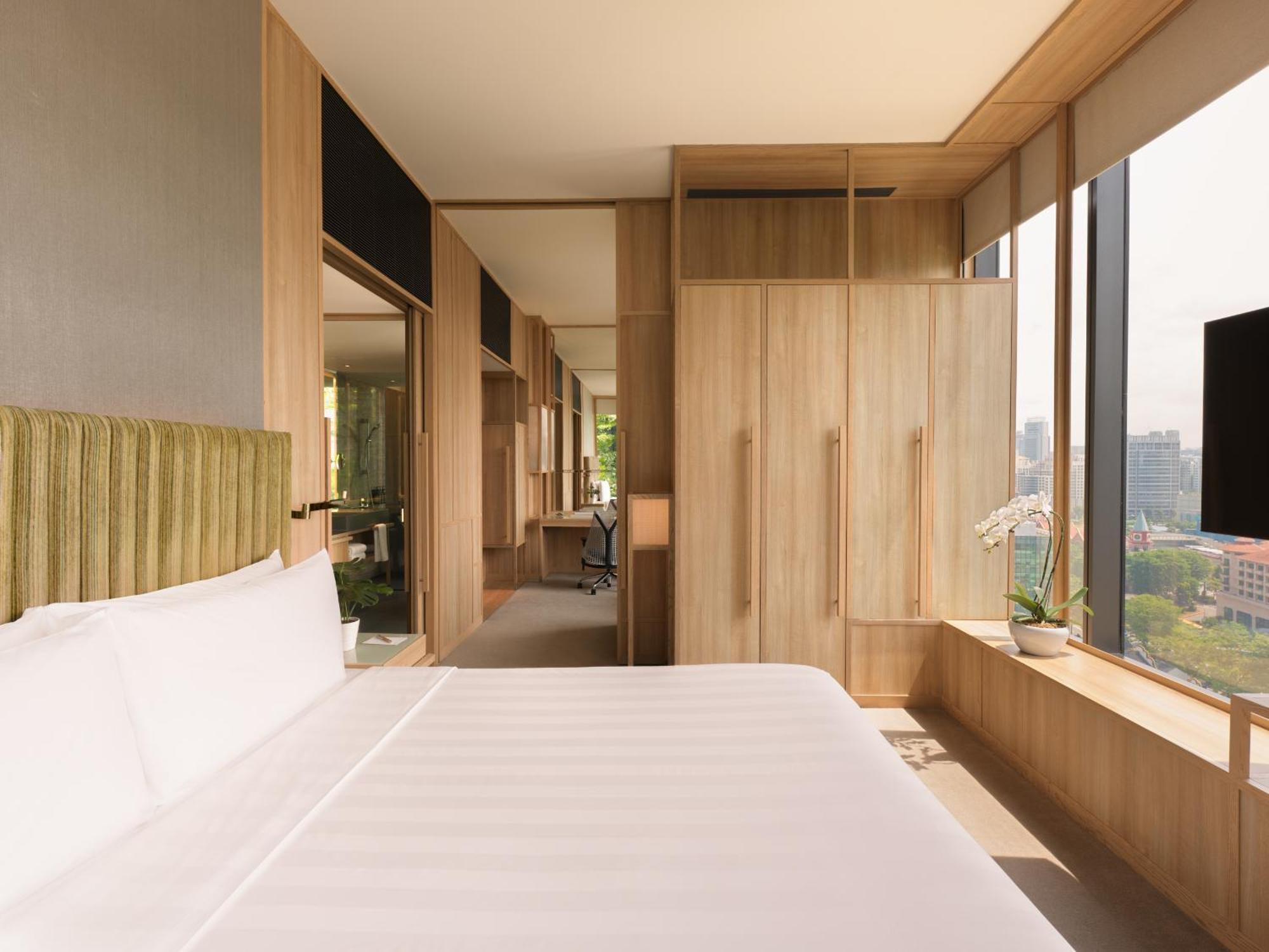Parkroyal Collection Pickering, Singapura Luaran gambar The photo shows a modern hotel room featuring a simple design with a focus on natural materials. There is a large bed with white bedding positioned against a wall, which has a textured green headboard. On one side of the room, there are wooden cabine