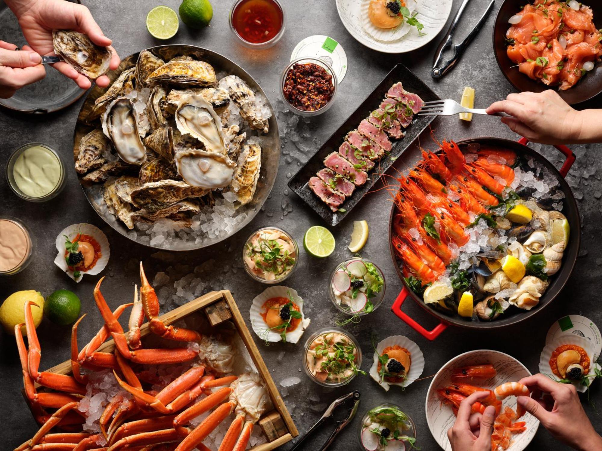 Parkroyal Collection Pickering, Singapura Luaran gambar The photo displays an elaborate seafood feast. Various dishes are arranged on a table, showcasing a variety of seafood:

1. **Oysters** on ice: A large platter holds several oysters, garnished with lemon slices.
2. **Crab legs**: A wooden crate is fi